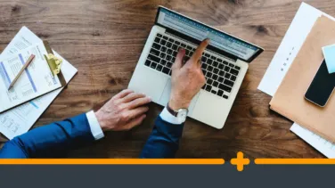 Ręce mężczyzny w garniturze pracującego na laptopie przy biurku z dokumentami i telefonem