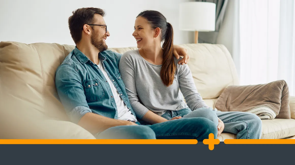 Uśmiechnięta para siedząca razem na kanapie w domowym wnętrzu