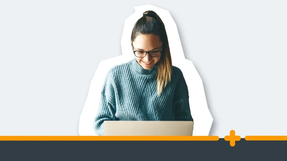 Młoda uśmiechnięta kobieta w okularach i swetrze pracująca przy laptopie