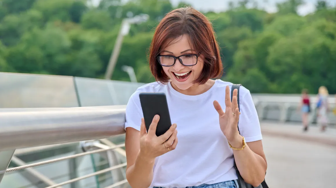 Zadowolona kobieta przegląda wiadomości na smartfonie na świeżym powietrzu