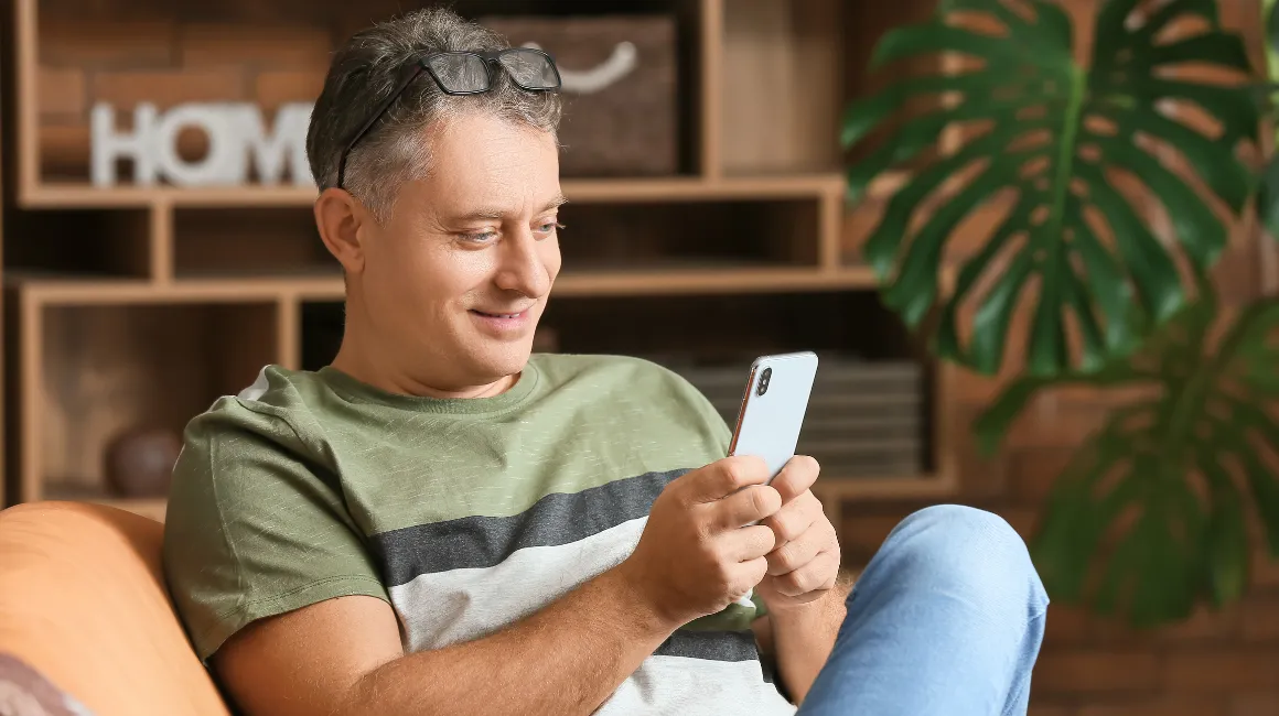 Zrelaksowany dojrzały mężczyzna korzystający ze smartfona w domowym zaciszu